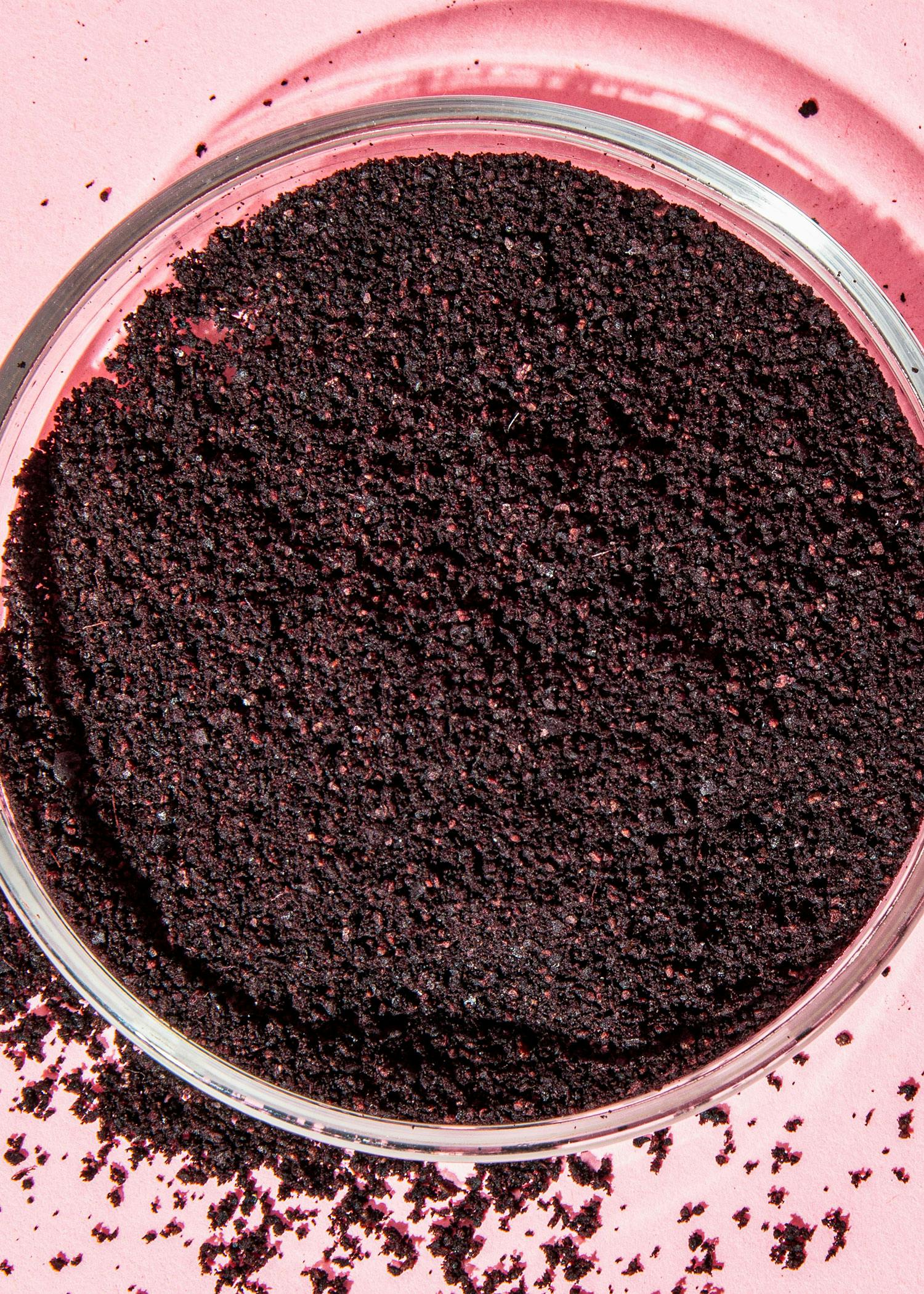 eine Nahaufnahme einer Glasschale mit schwarzem Pulver auf einem rosa Hintergrund