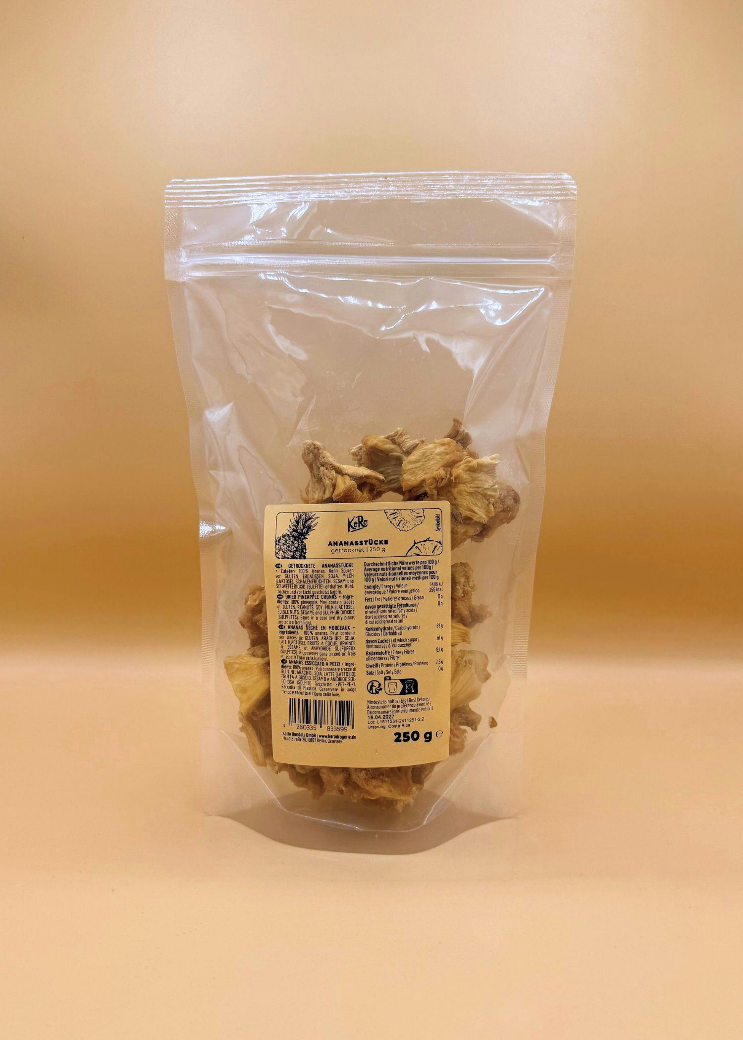 eine durchsichtige plastiktüte mit getrockneten ananasstücken und einem produktetikett, das nährwertangaben und zutaten zeigt, vor einem beigen hintergrund.