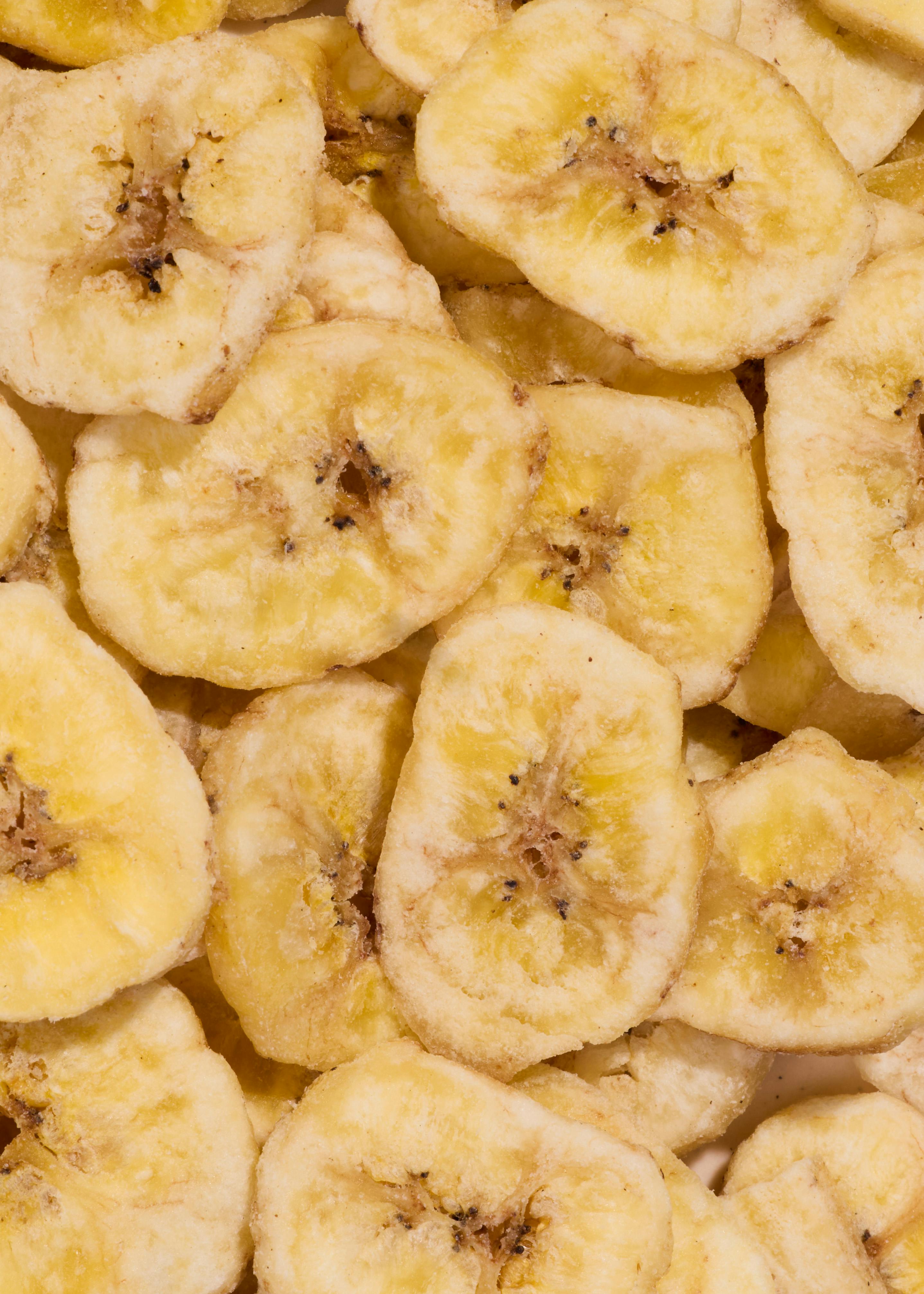 ein nahaufnahme von vielen hellgelben, getrockneten bananenscheiben mit dunklen kernen.