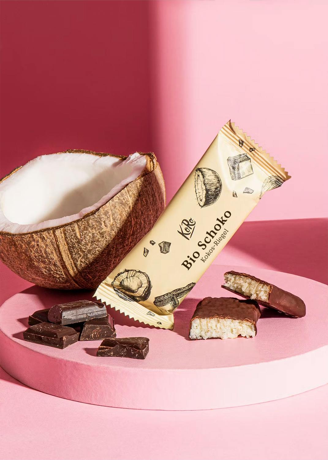 ein Bio-Schoko-Stick liegt auf einem rosa Tisch neben einer Kokosnuss