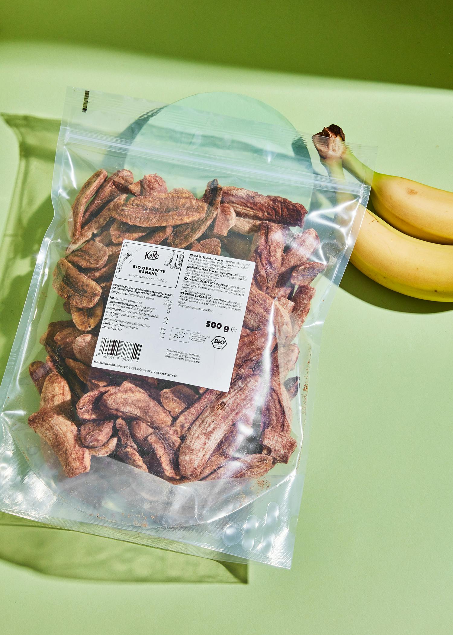 ein Plastikbeutel mit getrockneten Bananen steht neben zwei Bananen