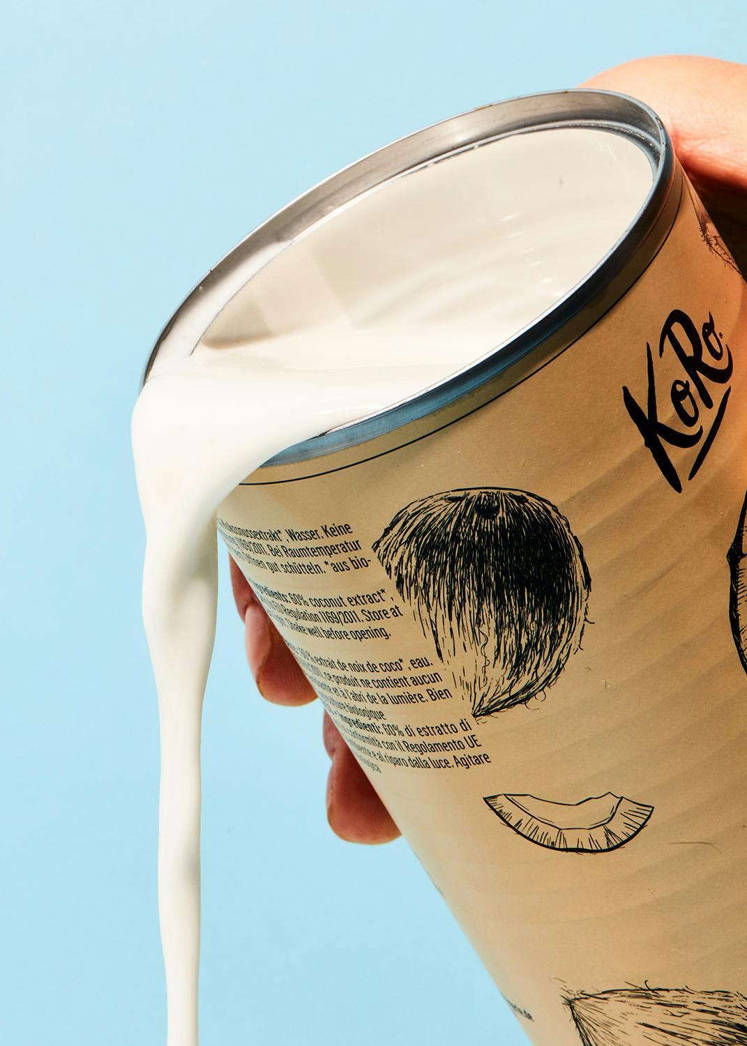 eine Person gießt Milch aus einer Dose mit der Aufschrift kora