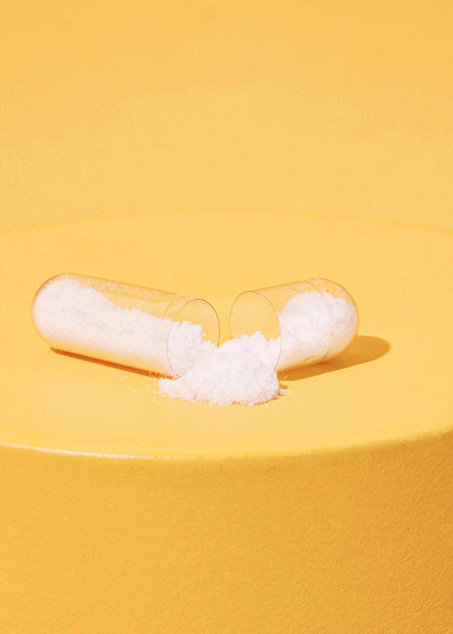 eine transparente Kapsel mit weißem Flüssigkeit darin auf einem gelben Tisch