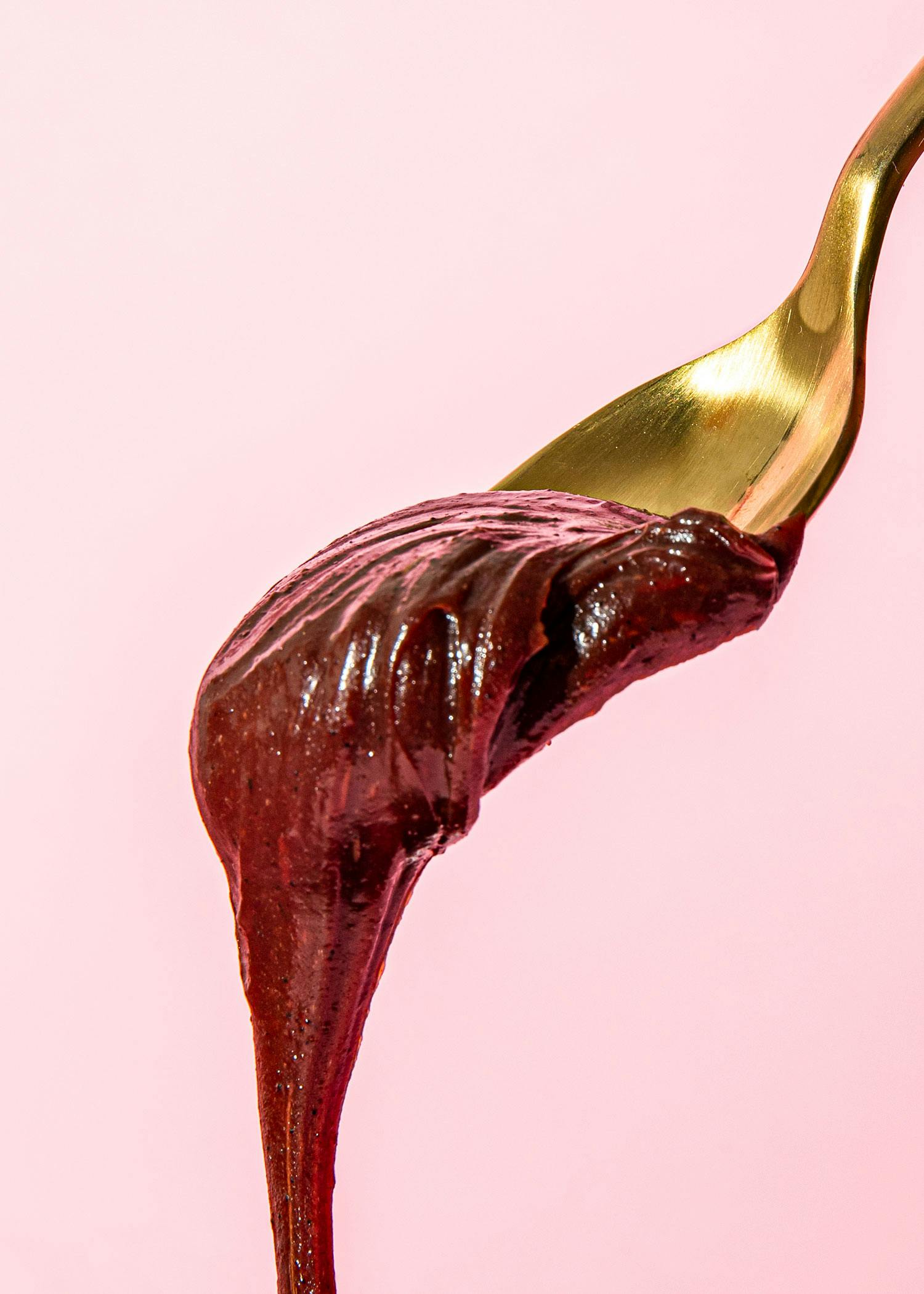 ein goldener Löffel mit Schokoladencreme auf einem rosa Hintergrund