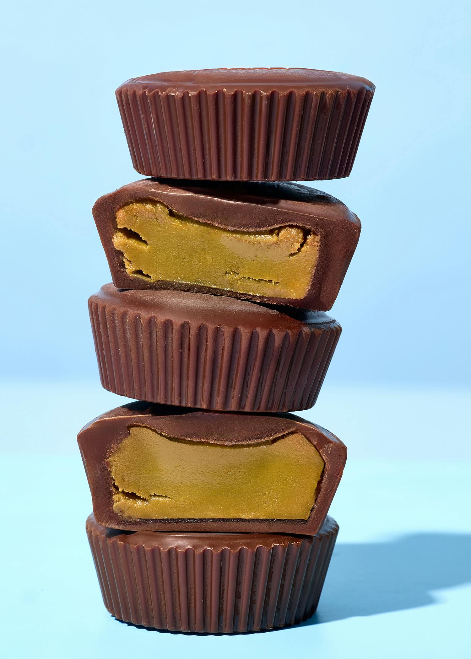 ein stapel aus vier schokoladen-erdnussbutter-bechern, von denen zwei aufgeschnitten sind und die erdnussbutterfüllung zeigen, vor blauem hintergrund.
