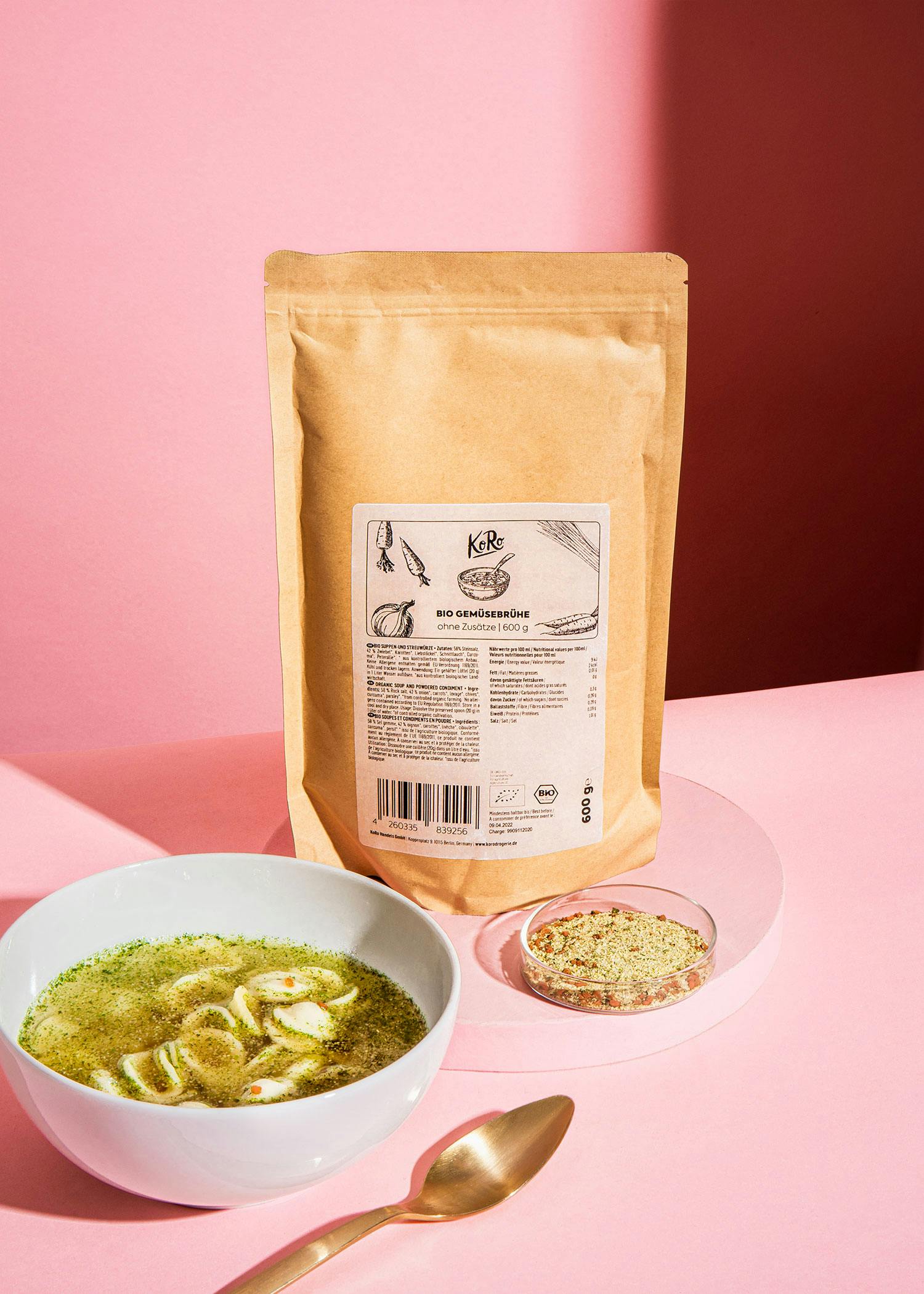 eine weiße Schüssel Suppe steht neben einer braunen Tüte mit Gemüsebrühe