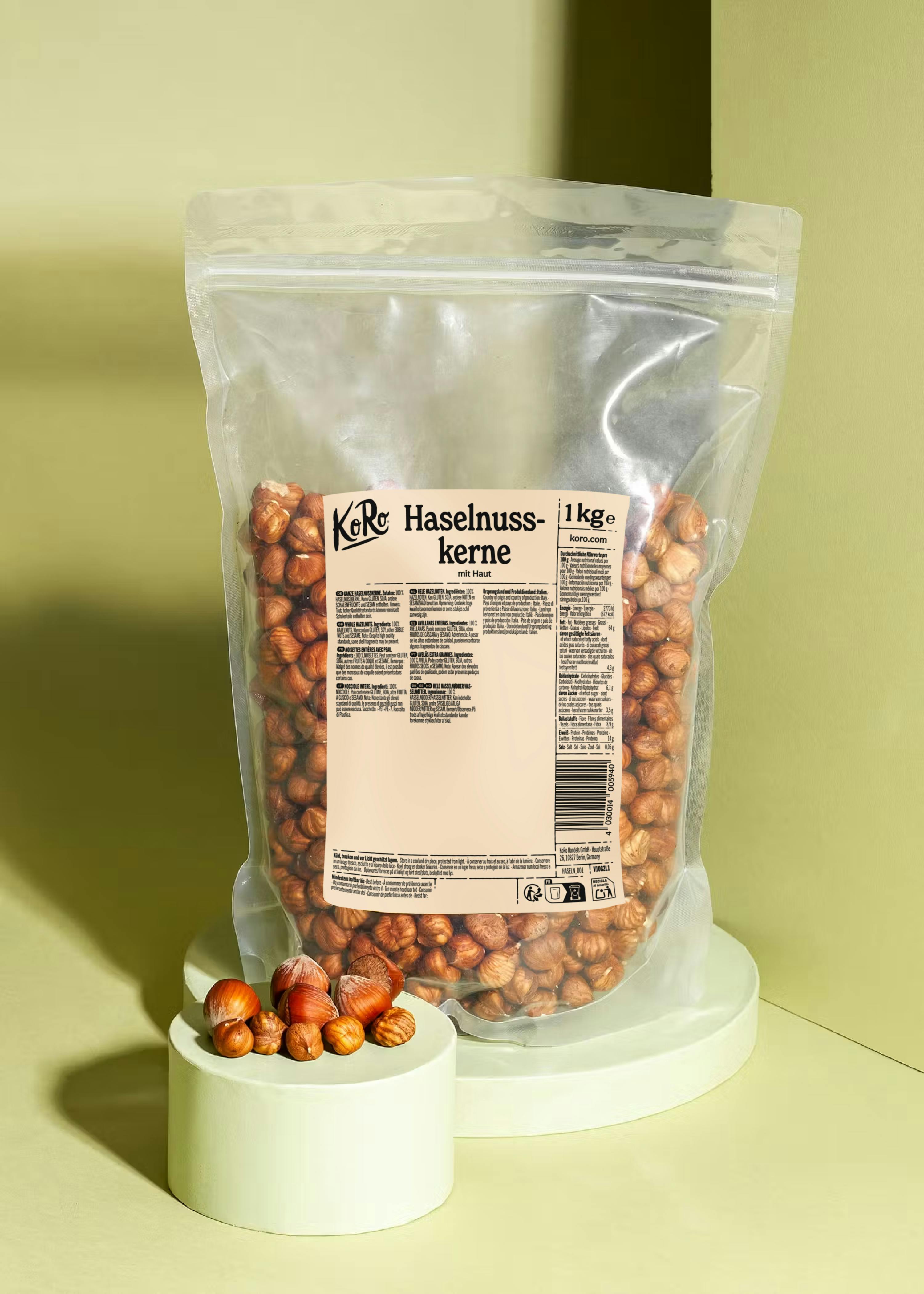 eine transparente verpackung mit 1 kg koro haselnusskernen mit haut steht auf einem hellgrünen podest, daneben liegen einige lose haselnüsse auf einem kleineren podest.