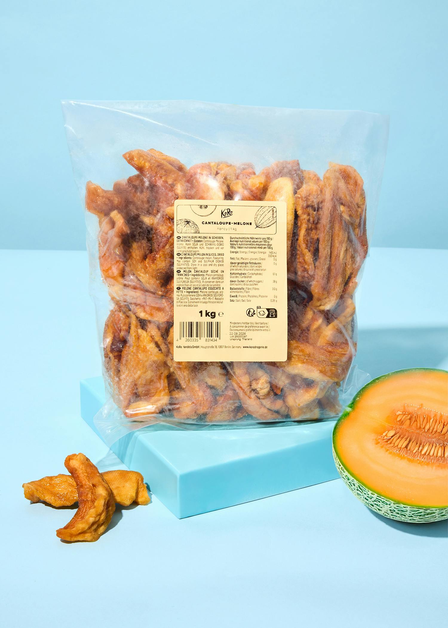 eine durchsichtige tüte mit getrockneten cantaloupe-melonenscheiben und einem etikett, daneben liegen einige scheiben und eine halbe frische cantaloupe-melone auf einem hellblauen untergrund.