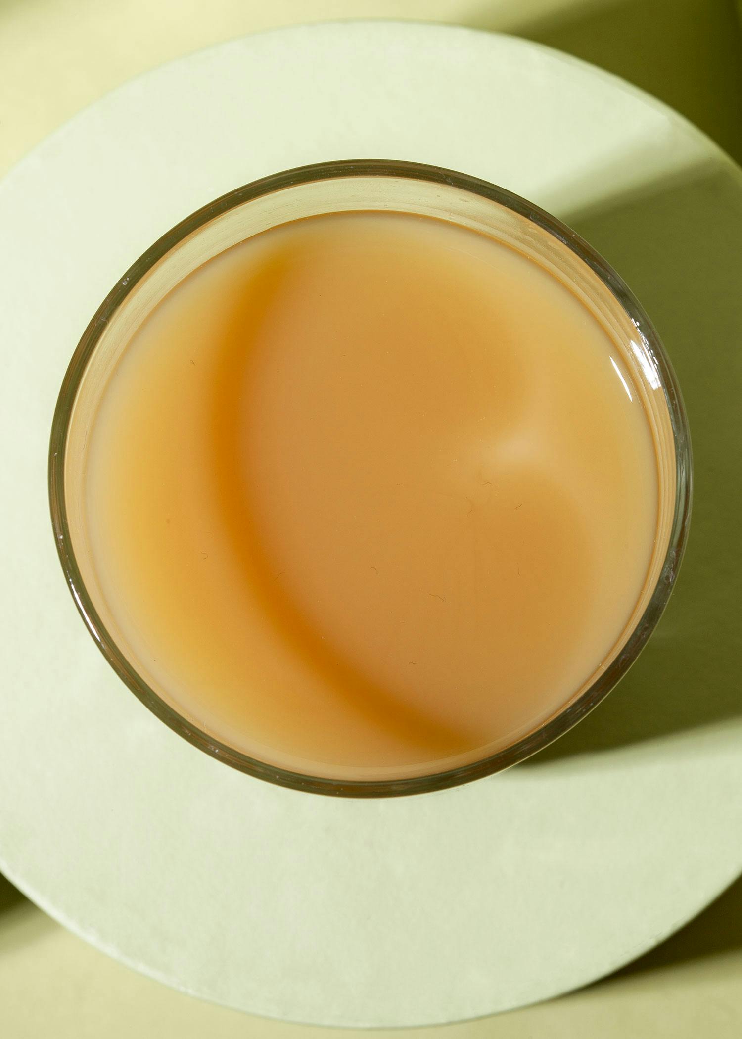 ein Glas gefüllt mit einem hellbraunen liquid auf einem weißen Teller