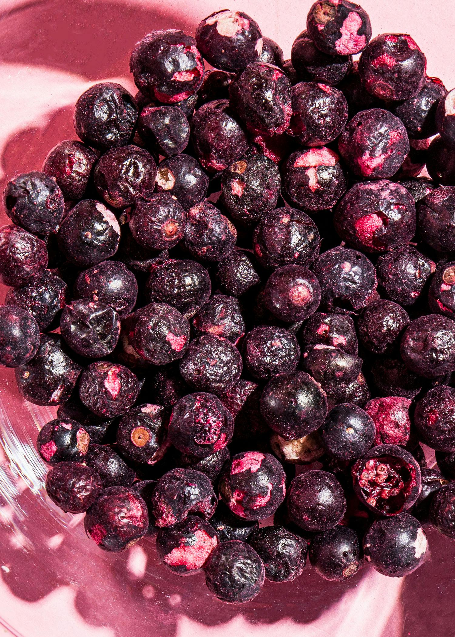 eine Glasschüssel mit gefrorenen Blaubeeren auf rosa Hintergrund