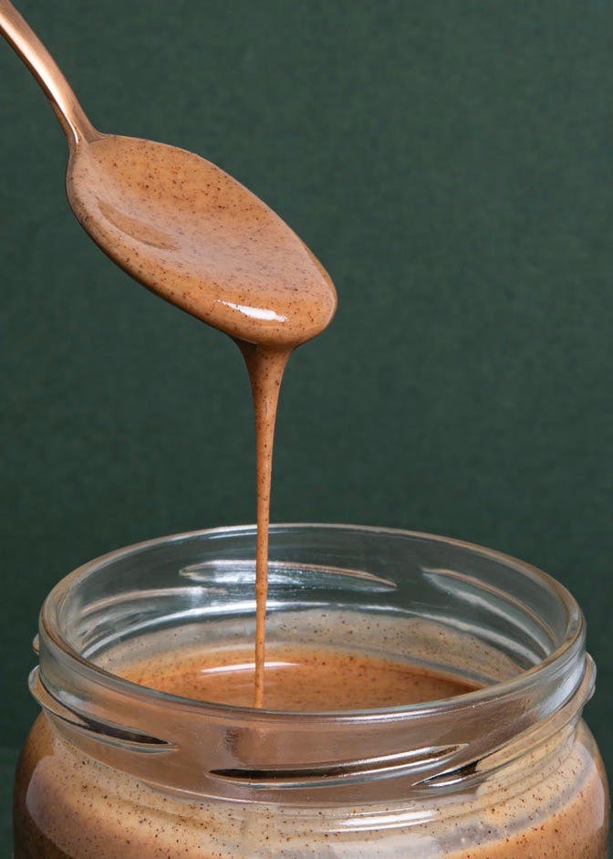 ein Glas Erdnussbutter wird mit einem Löffel aus dem Glas gegossen