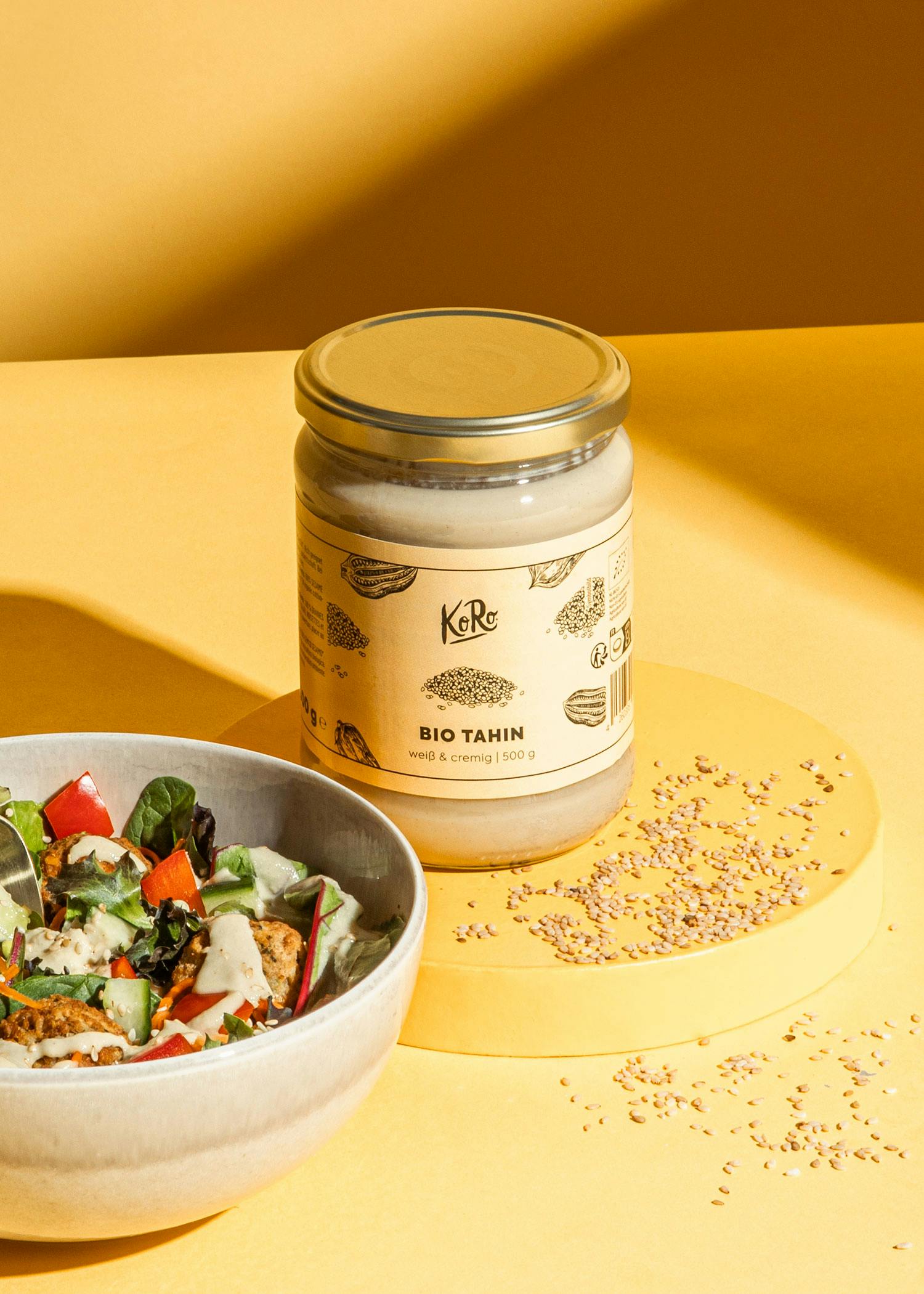 eine schüssel mit salat neben einem glas bio tahin