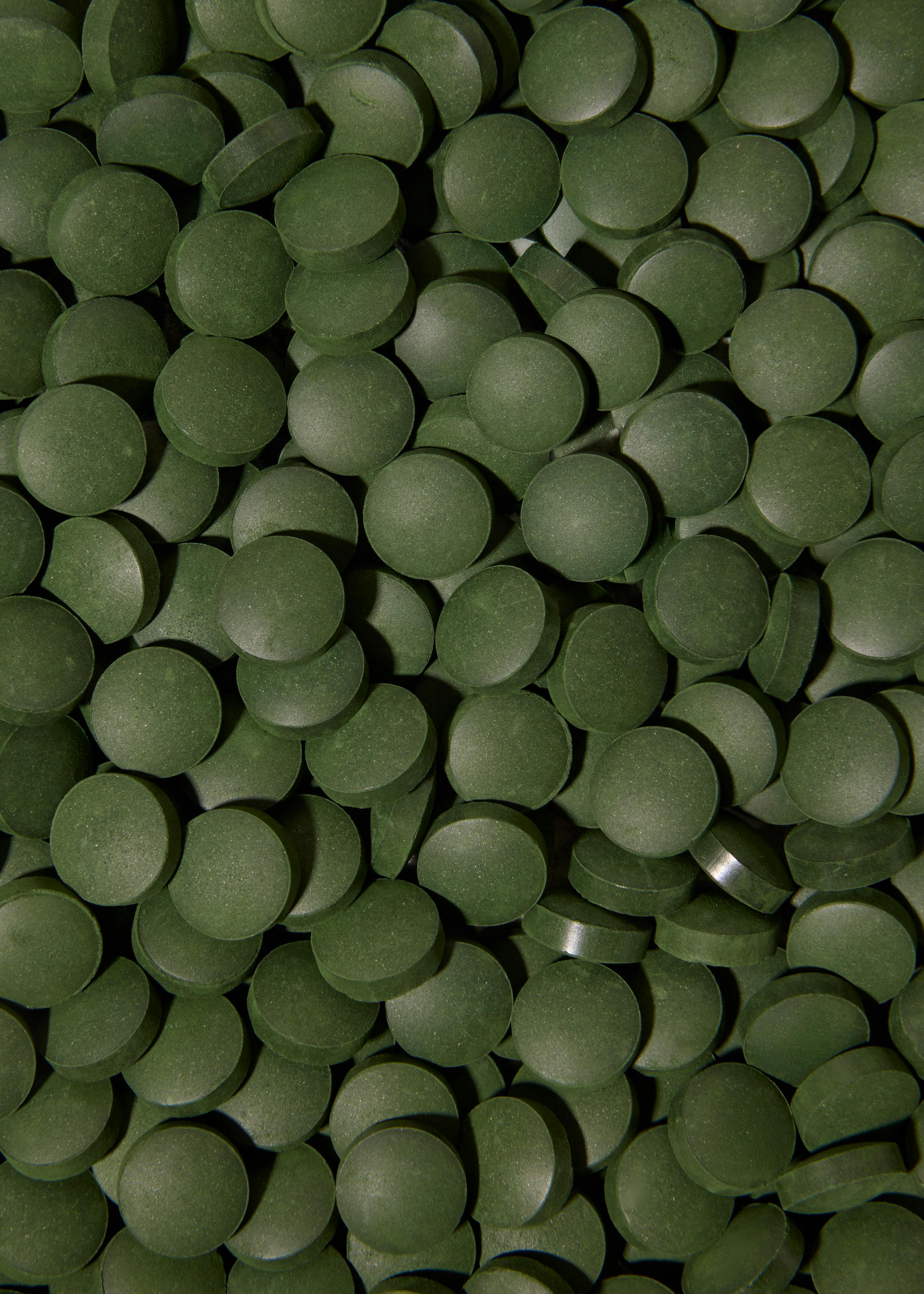 eine nahaufnahme vieler kleiner, runder, dunkelgrüner tabletten, die den bildausschnitt füllen.