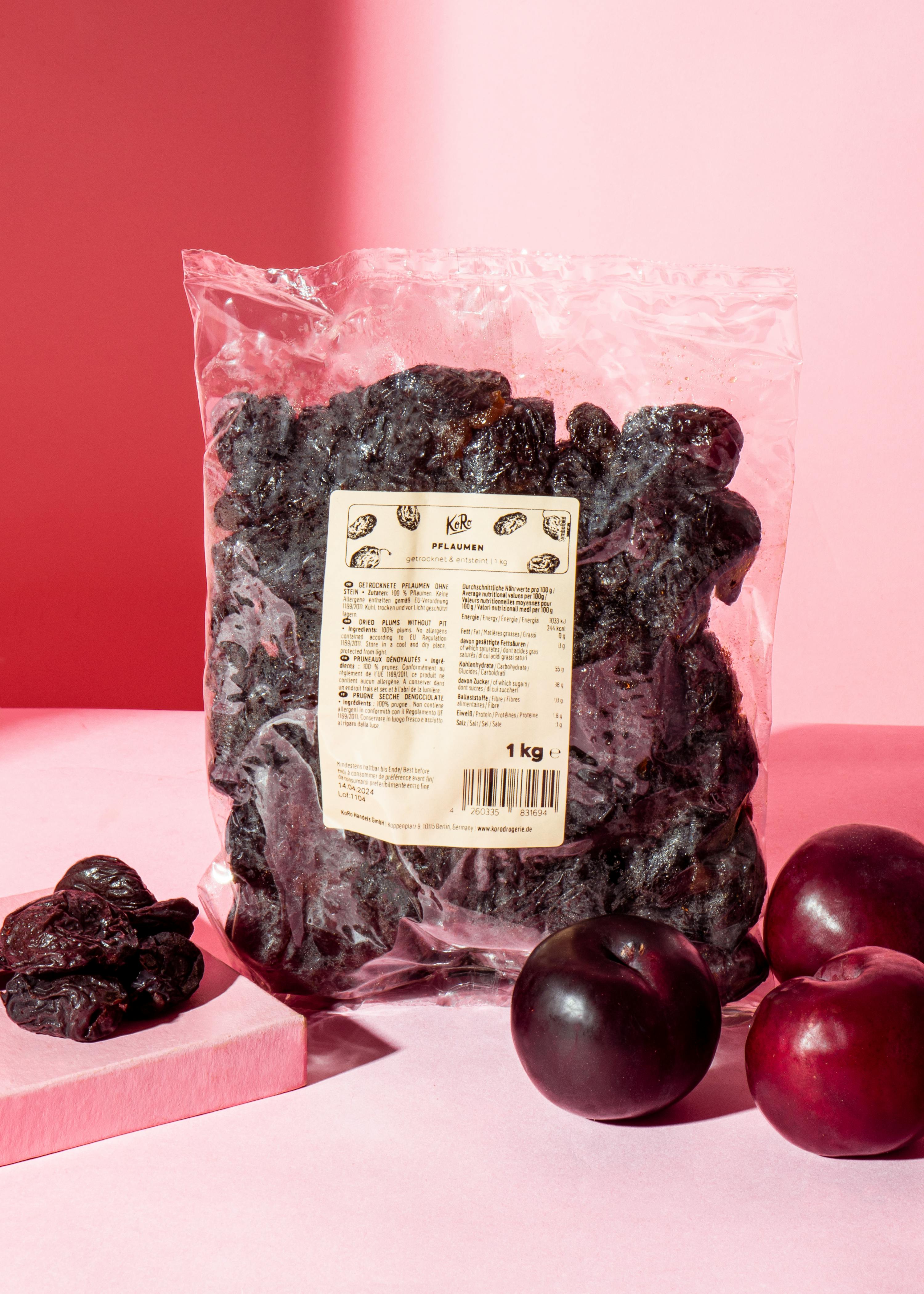 eine Tüte getrocknete Pflaumen steht neben einem Haufen Pflaumen