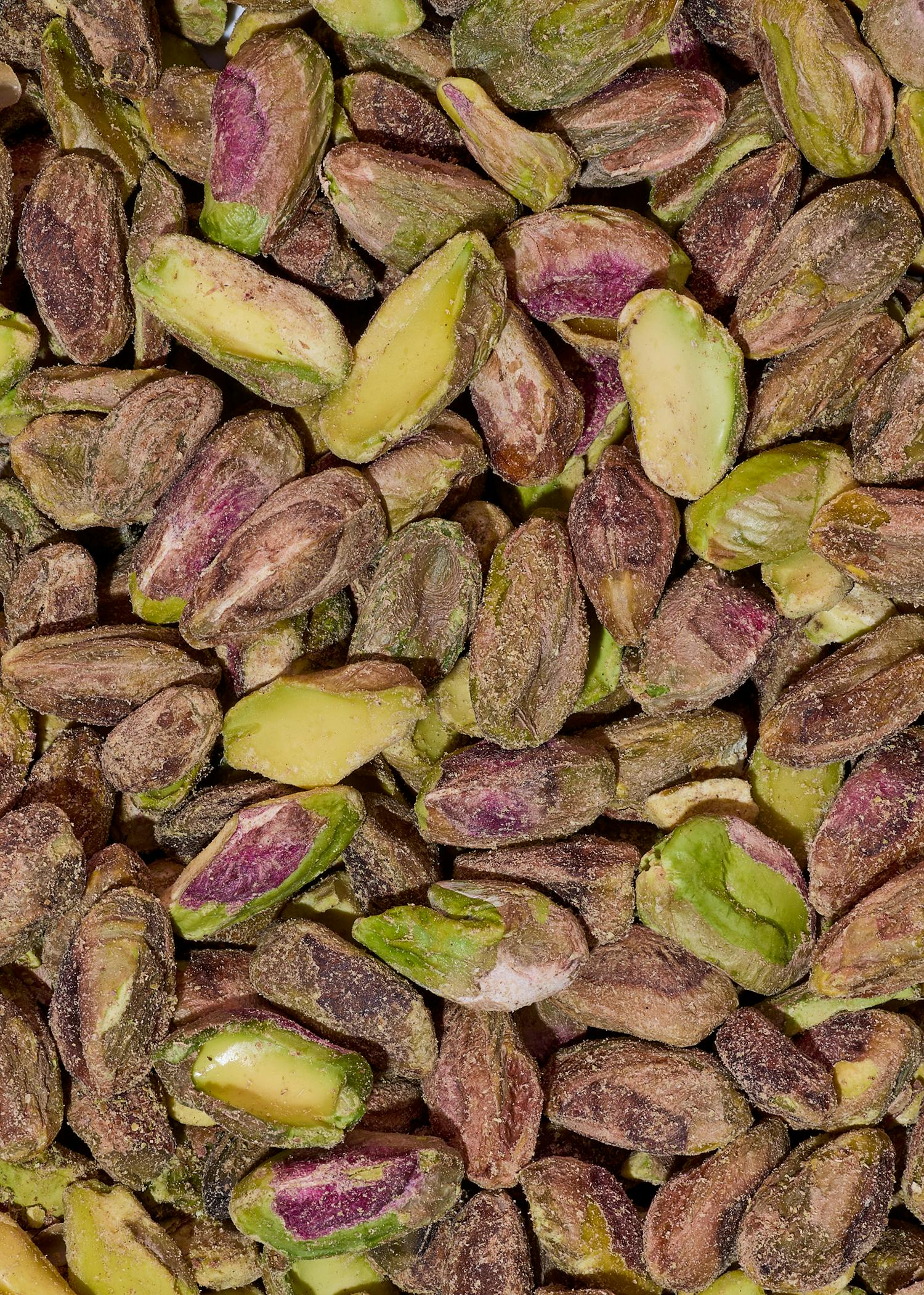 nahaufnahme von vielen geschälten pistazien mit grünen und violetten kernen.