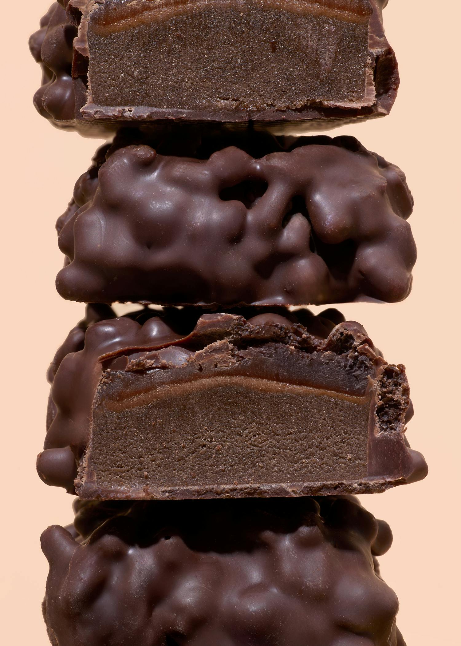 ein stapel aus vier schokoladenbonbons, von denen zwei aufgeschnitten sind und eine dunkle schokoladenfüllung mit einer dünnen karamellschicht zeigen, auf einem hellbeigen hintergrund.