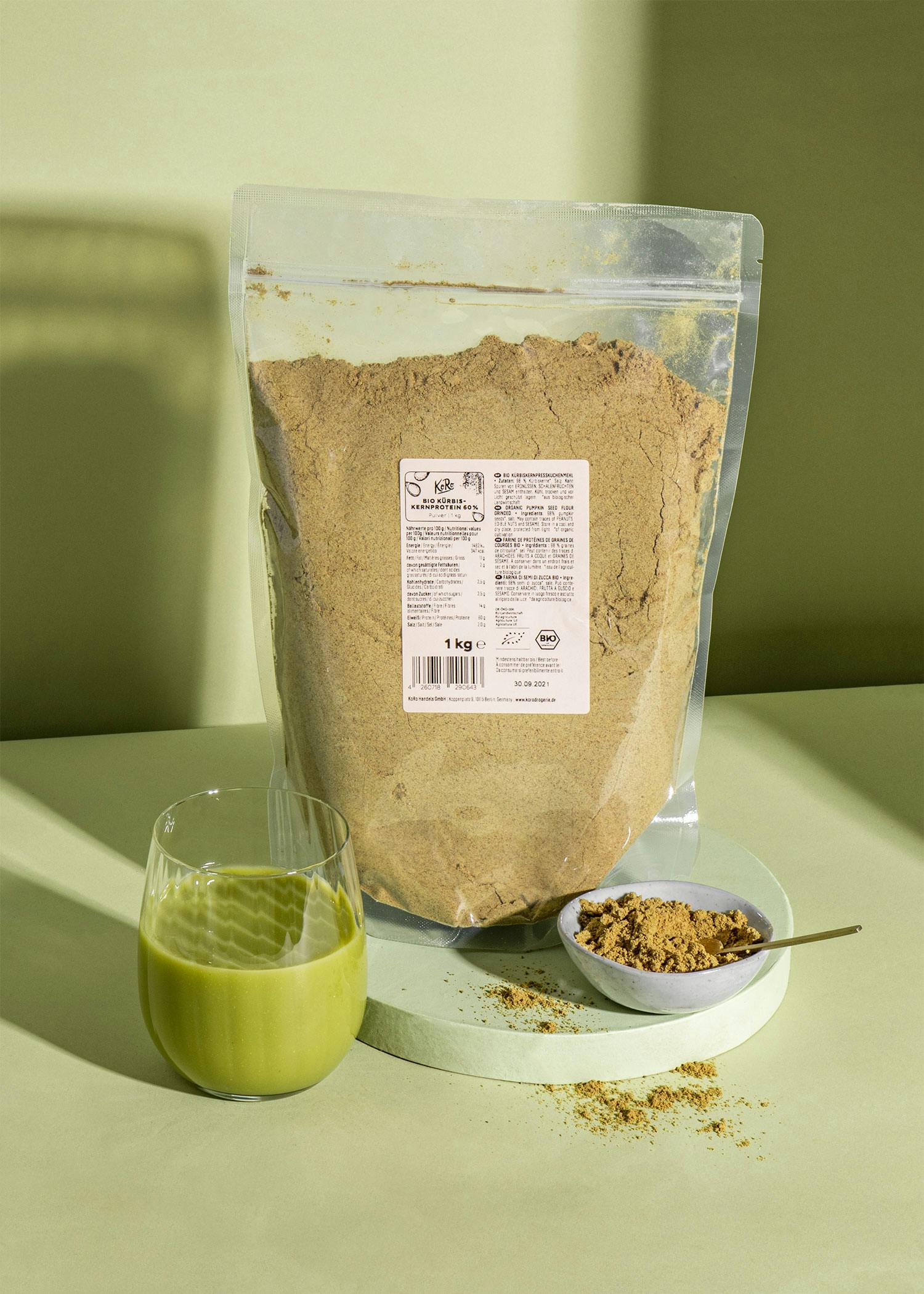 ein Glas grünen Smoothie steht neben einem Plastikbeutel mit braunem Pulver