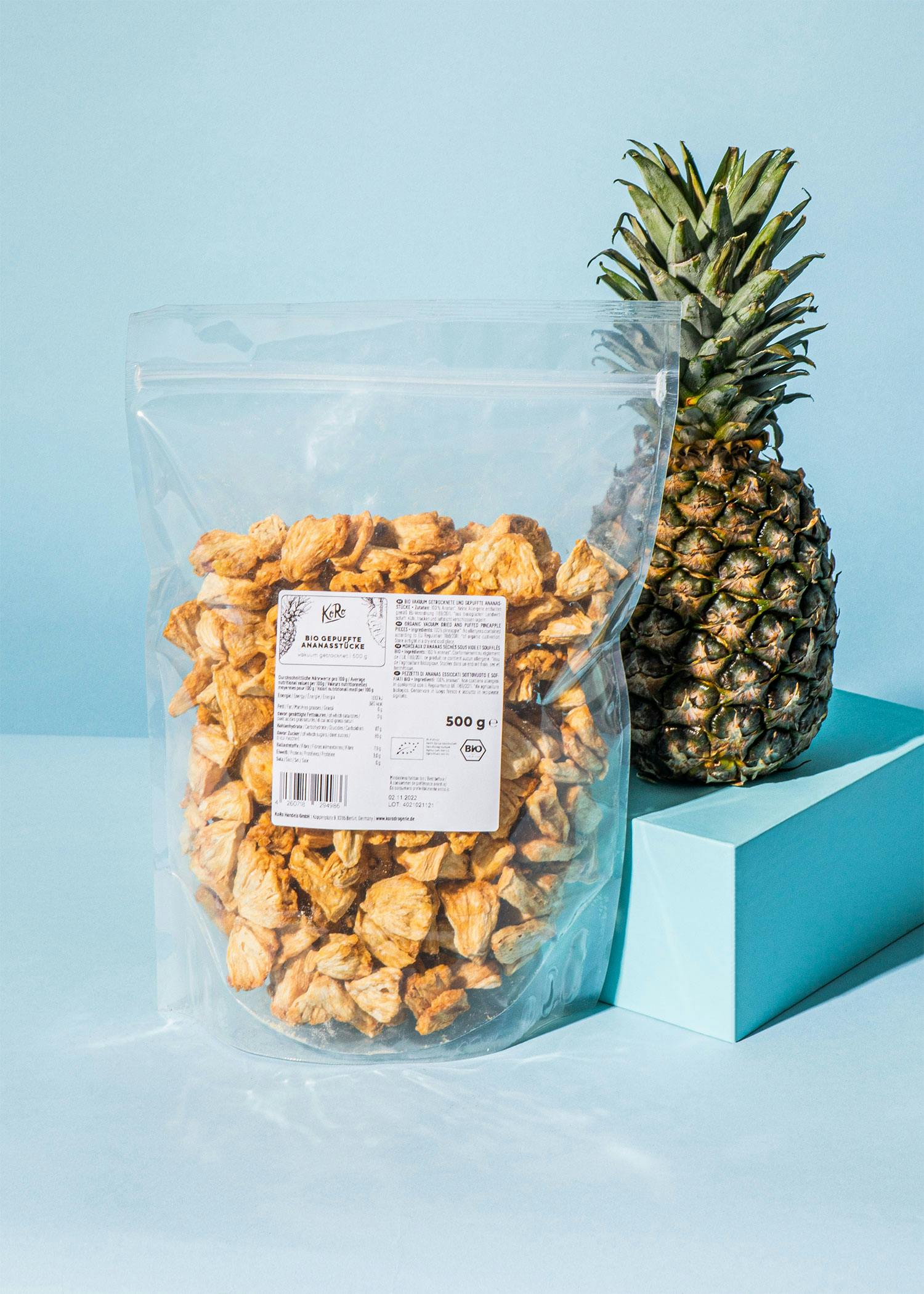 ein Plastikbeutel mit 500 g getrockneter Ananas steht neben einer Ananas