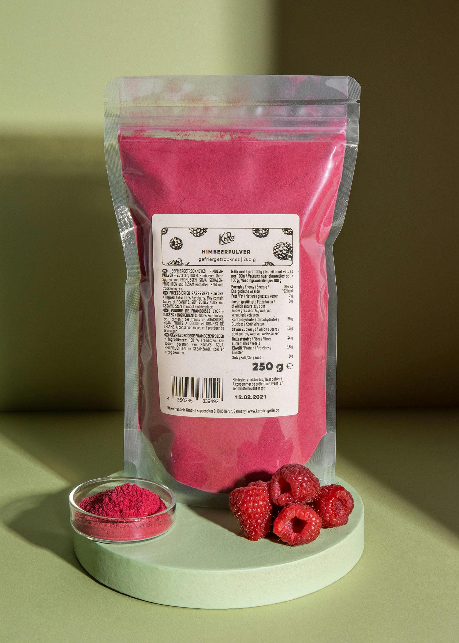 eine Packung Himbeerpulver steht auf einem Tisch neben frischen Himbeeren
