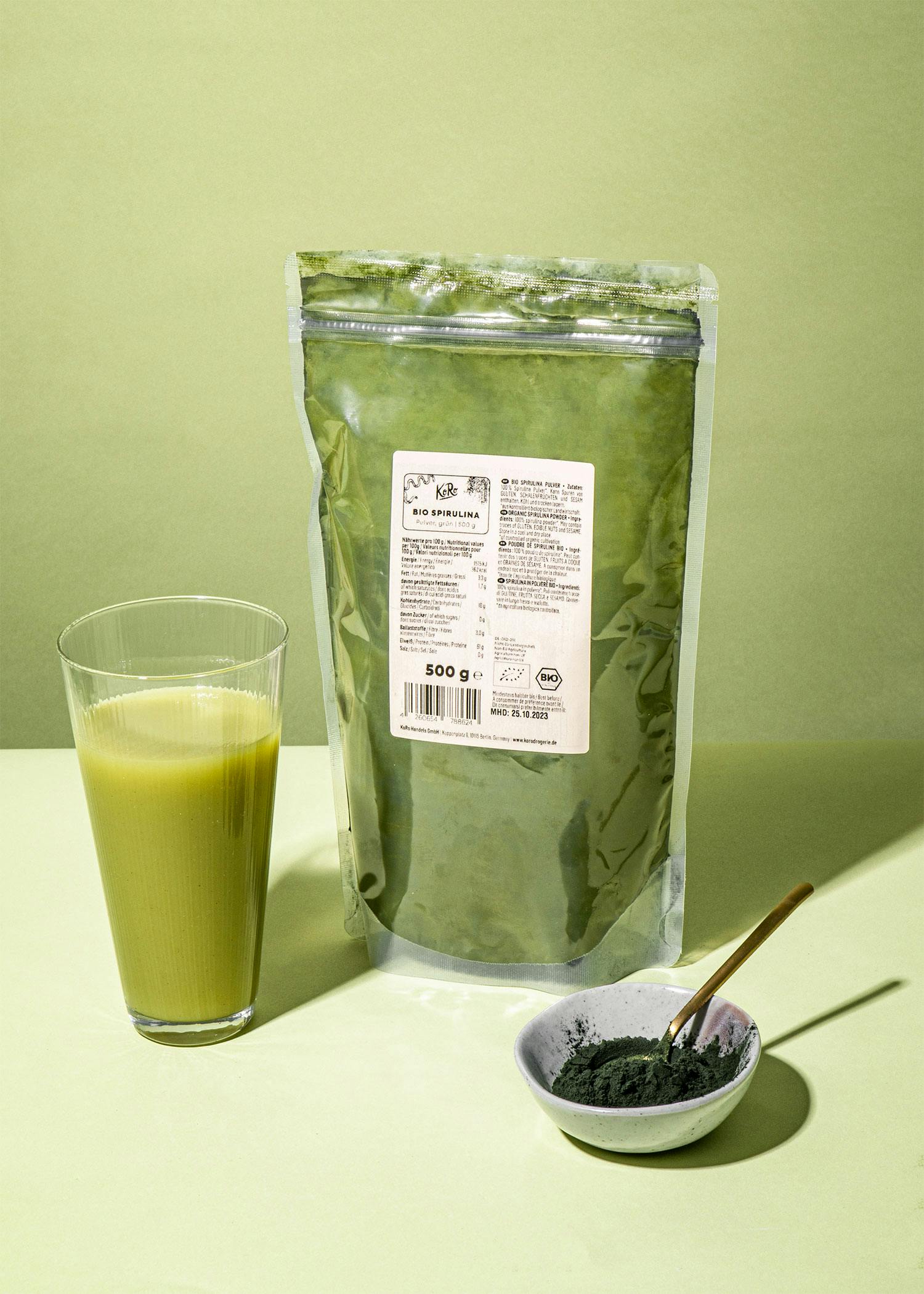 ein Glas und eine Tüte Bio-Spirulina-Pulver nebeneinander
