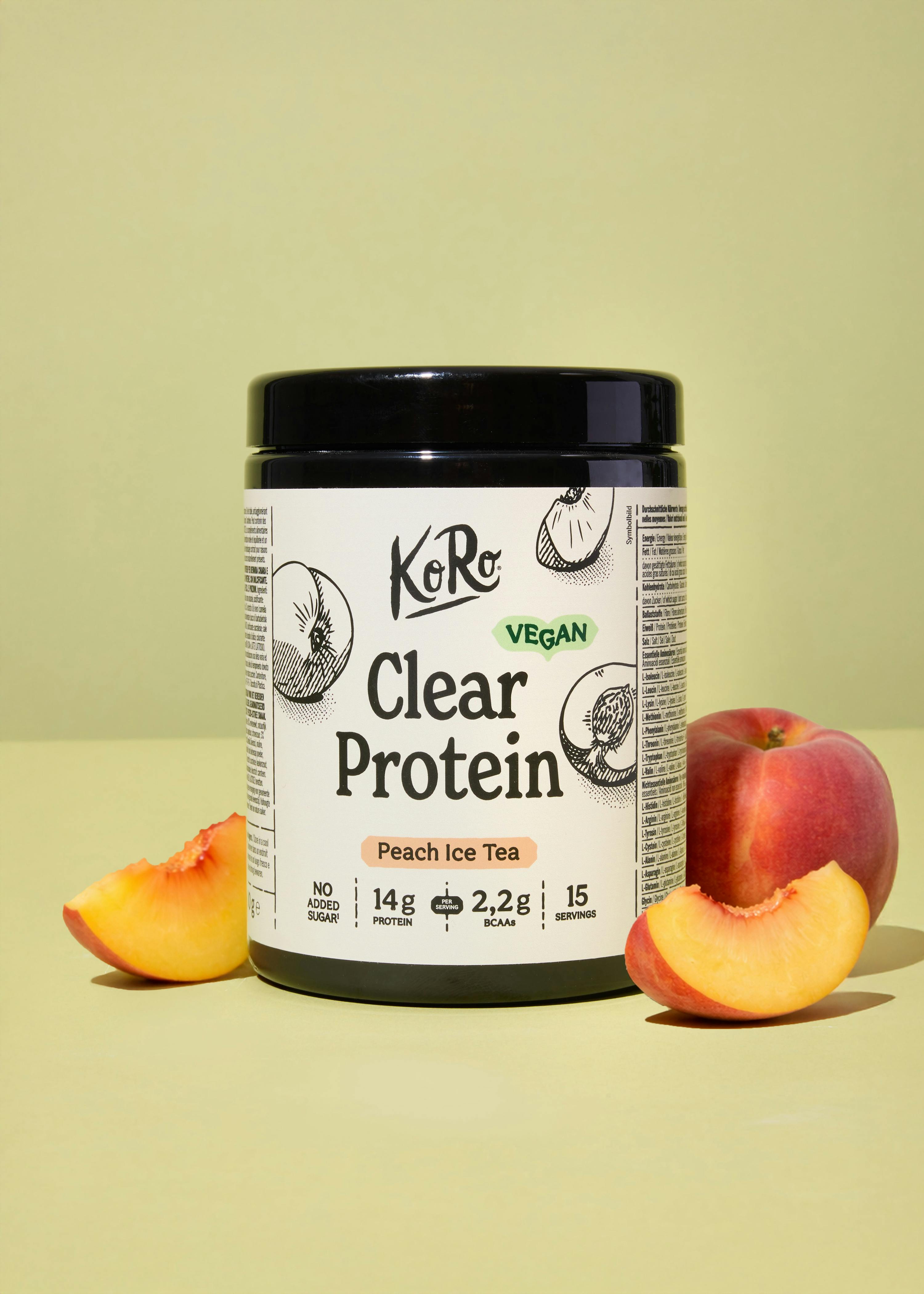 eine weiße dose koro clear protein pfirsich eistee, vegan, mit 14g protein und 2,2g bcaas pro portion, steht neben einem ganzen pfirsich und zwei pfirsichspalten auf hellgrünem hintergrund.